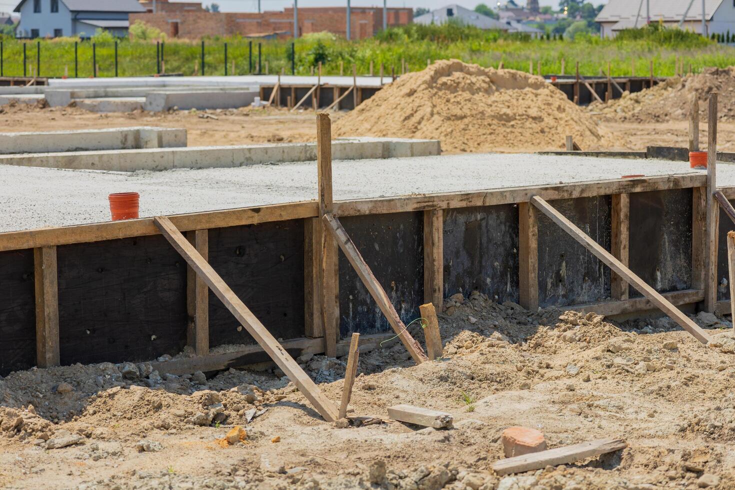 Workers are preparing a concrete foundation for a new residential building, with wooden supports installed and sandy terrain surrounding the area photo