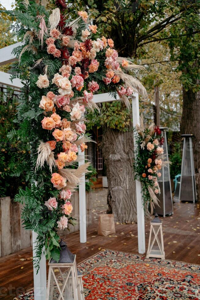 Outdoor rustic wedding floral arch with autumn roses and greenery photo