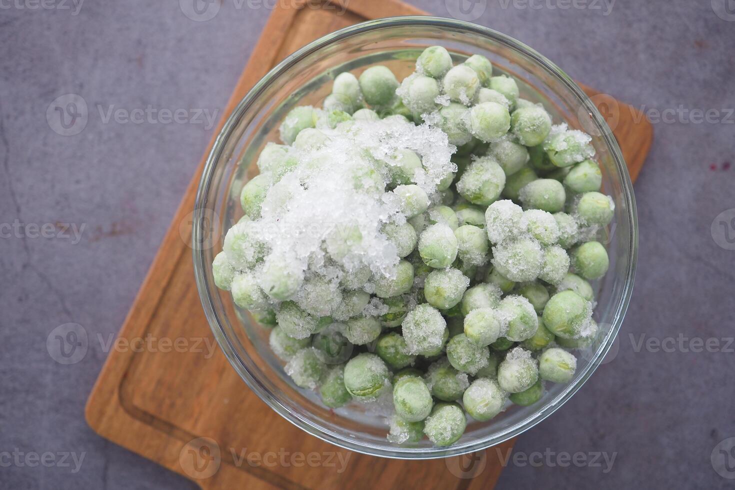 Frozen green peas in a glass bowl on a wooden cutting board photo