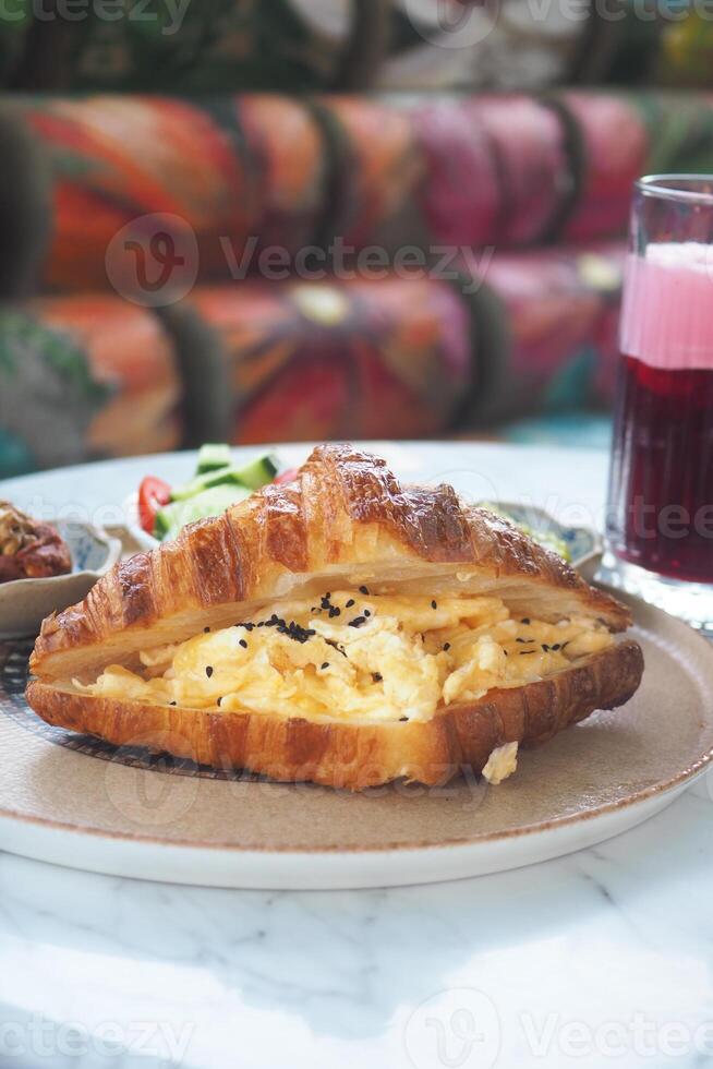 Delicious croissant sandwich with eggs and drink on table photo