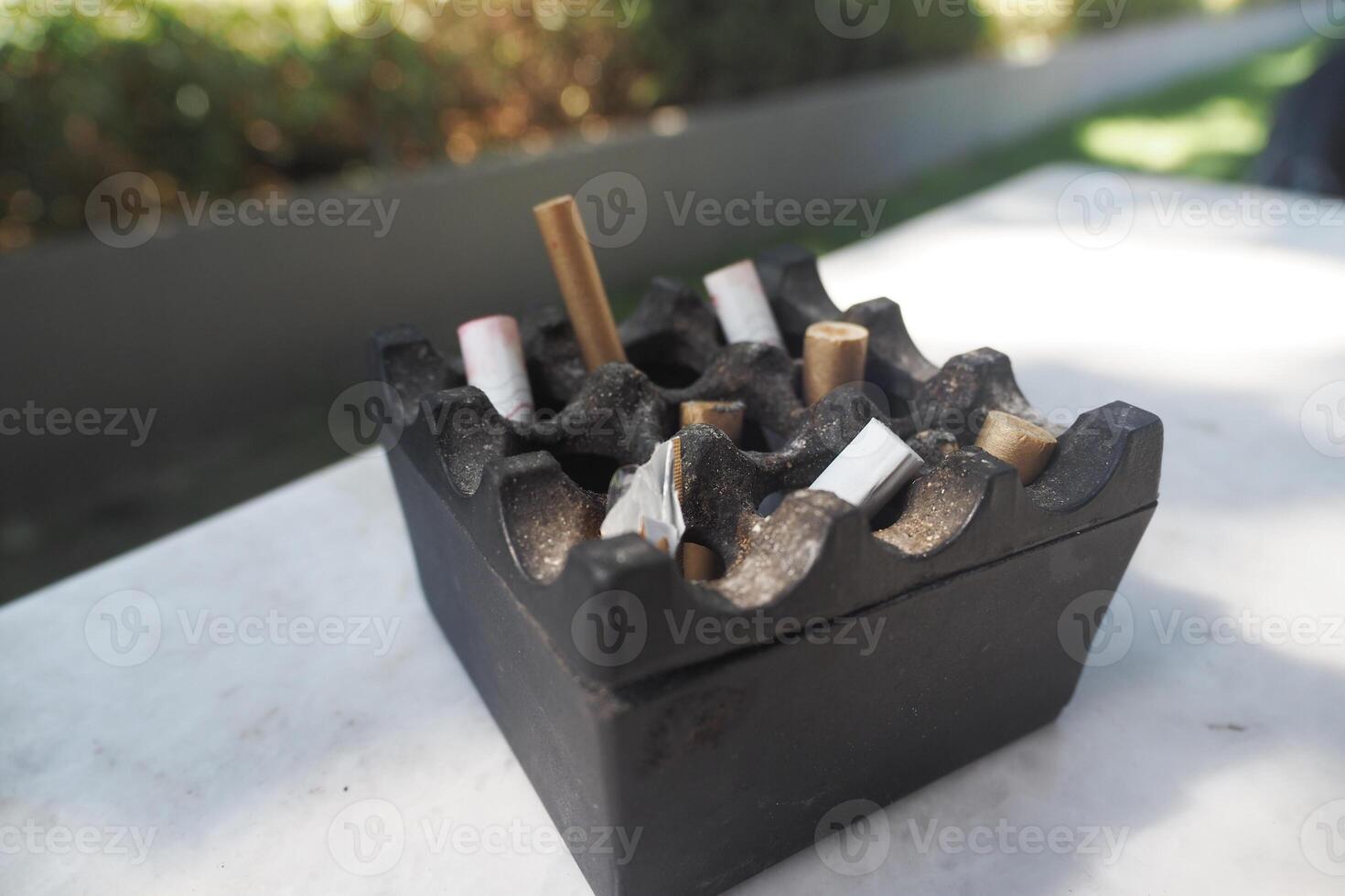 Ashtray filled with cigarette butts on an outdoor table photo