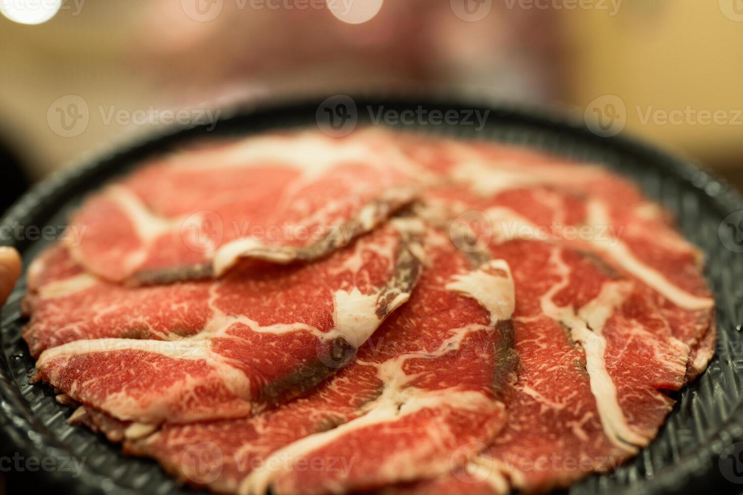 Thinly sliced beef arranged on a black tray, perfect for hot pot. photo