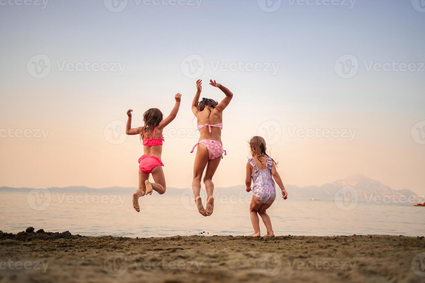 Joyful sisters jumping on the beach at sunset by the water photo