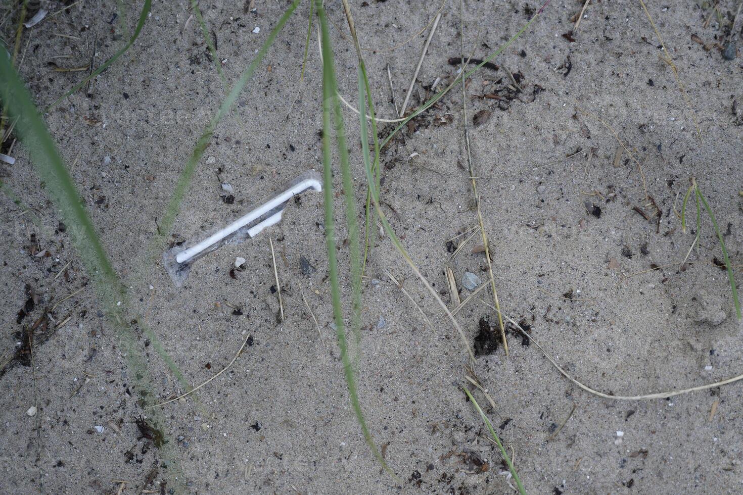 A still wrapped and unused straw lies on the beach among the grains of sand and dirt photo