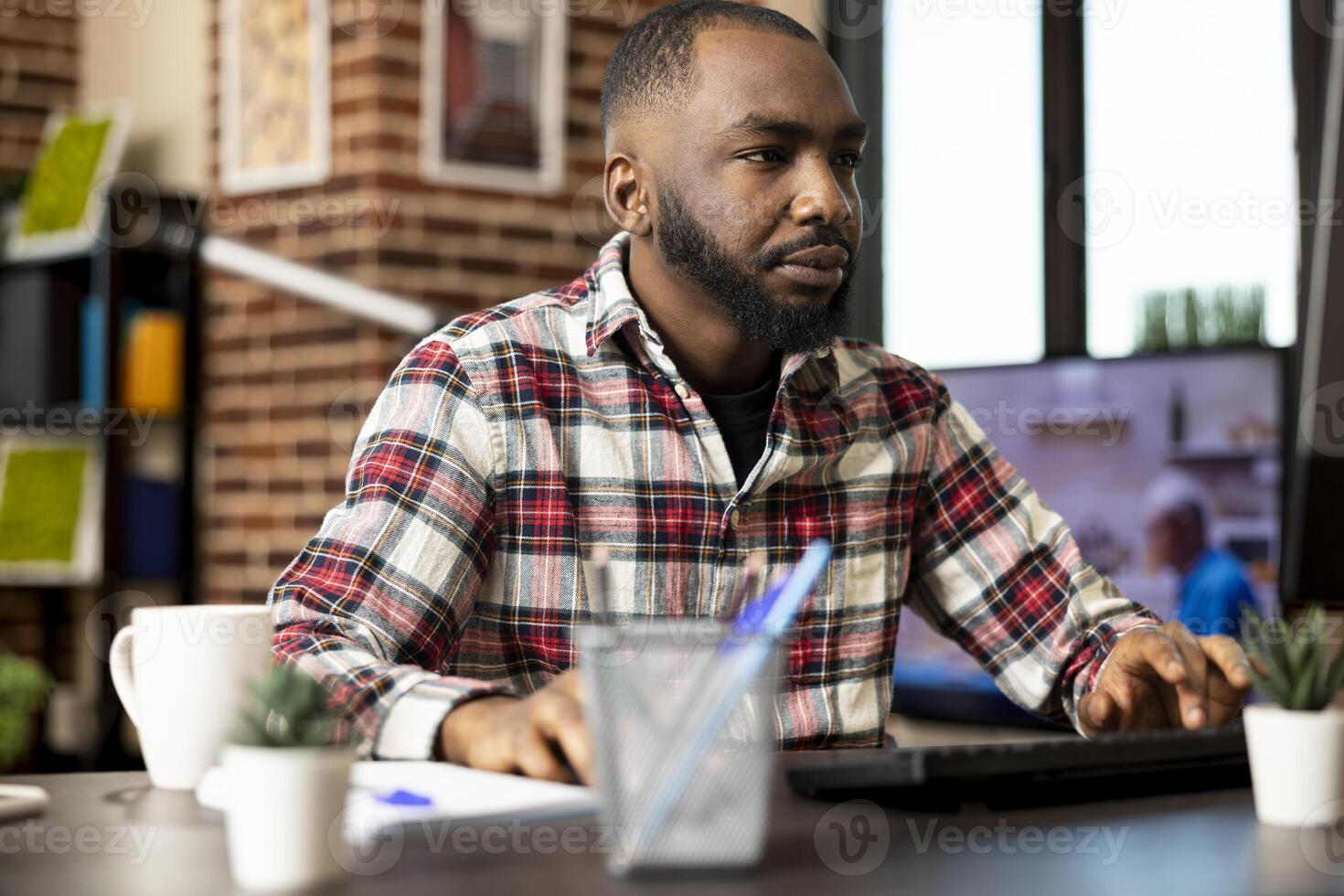 Focused black man working from home, reviewing company records on desktop pc. African american entrepreneur with hands on keyboard and mouse, updating business fiscal reports before deadline. photo