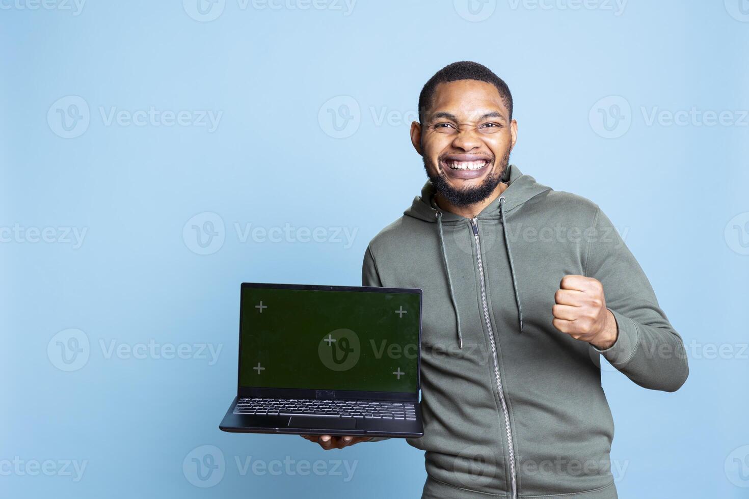 Young friendly african american guy feeling positive next to copy space mockup, gesturing for an advertisement against blue background. Male model with a hoodie smiling in studio. photo