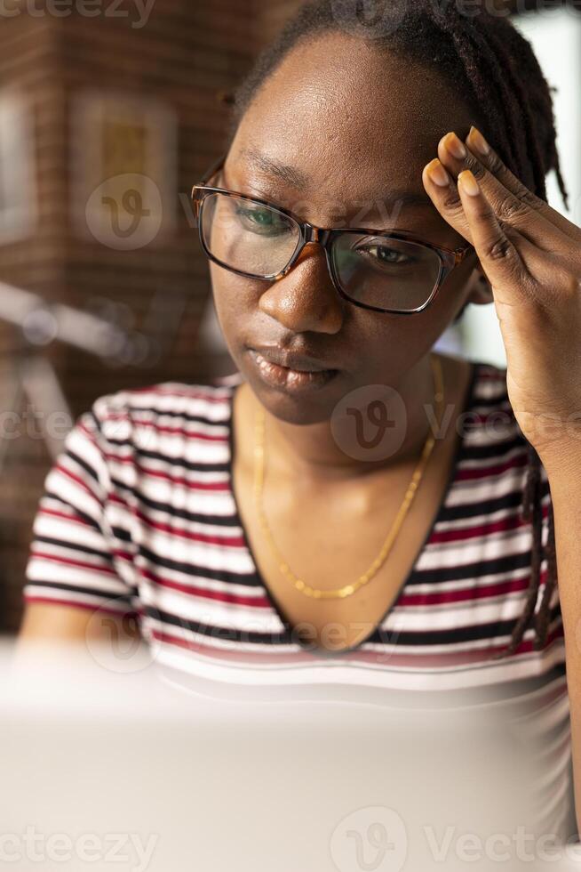 Female entrepreneur experiences headache while seated at home office desk, trying to manage multiple projects. Close up of fatigued woman massaging her temples, struggling to focus on laptop. photo