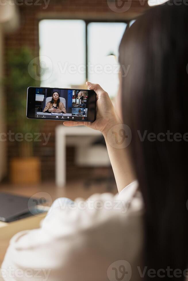 Female manager using cellphone to communicate with remote colleagues. Self employed woman seated at home with digital device, contributing to professional conversation remotely. photo