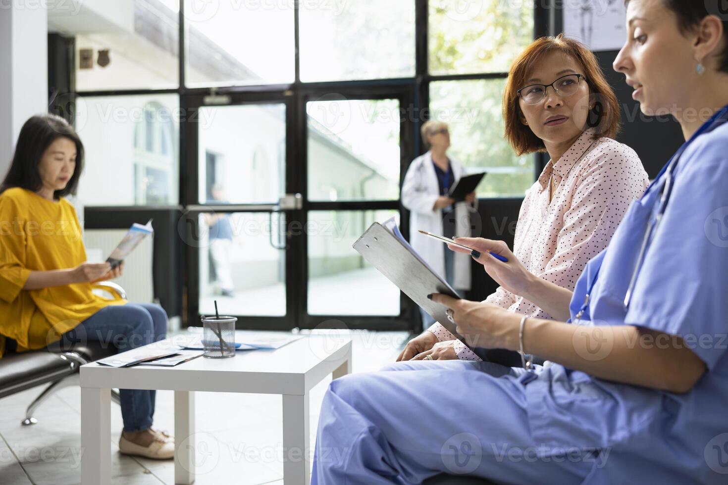 Medical assistant provides support and assistance to asian woman during routine checkup in hospital lobby. Discussion about prevention, medical tests and scheduling future appointments. photo