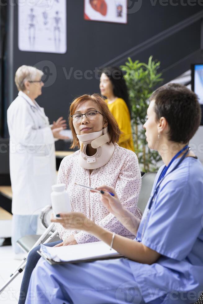 Medic provides strong painkillers for woman with neck fracture and cervical brace, checking condition of patient after cervical injury during checkup. Pain management and physiotherapy progress. photo