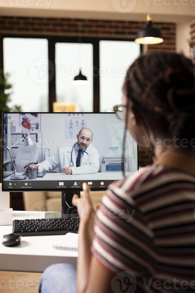 Close up of female patient attending virtual medical consultation at home. Computer screen shows caucasian male doctor speaking with black woman during online healthcare appointment. photo