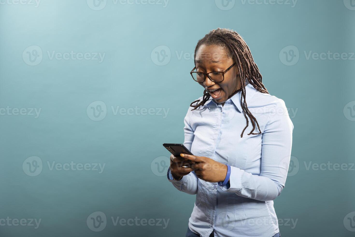 Shocked black woman staring at her smartphone, with mouth wide open, reacting to wonderful news. Excited african american lady, checking her mobile device, receiving surprising message, lottery win. photo