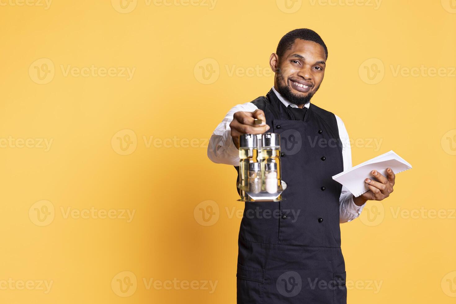 Restaurant employee with apron and cruet set takes orders from clients, writing down meal information on a notebook for customer satisfaction. Caterer butler in service oriented industry. photo