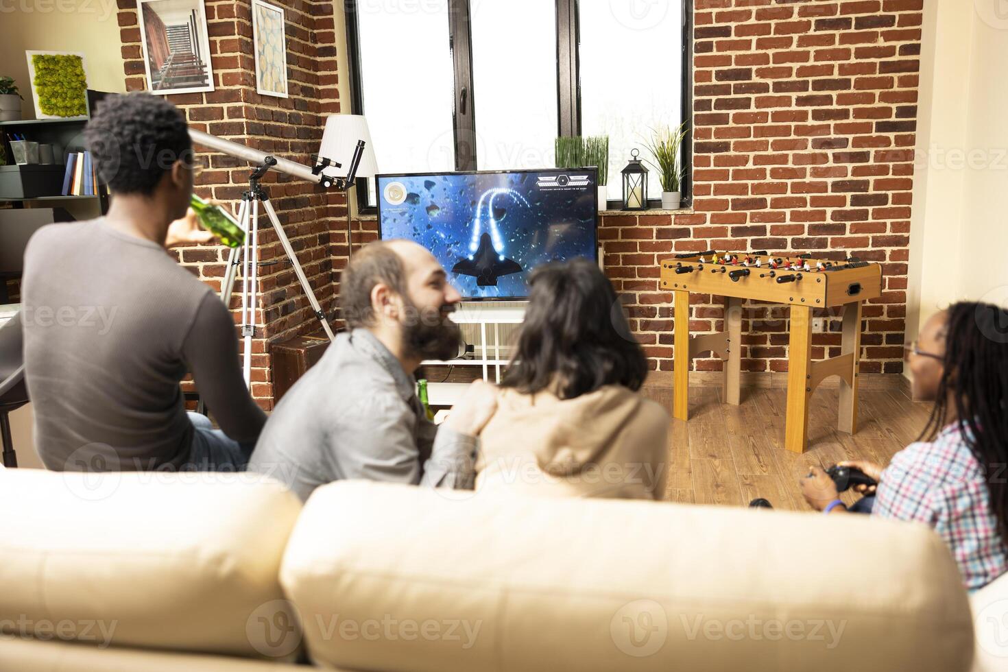 Young diverse adults seated on couch, some holding game controllers while others chat, hanging out in cozy living room. Group of friends playing games, socializing, and relaxing together. photo