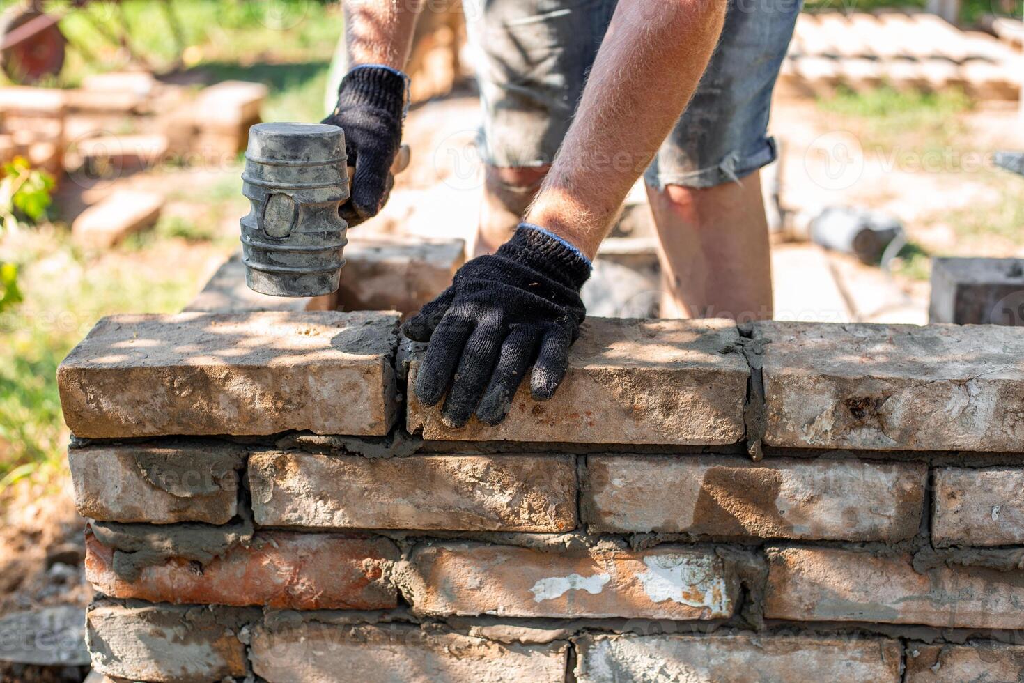 A worker wearing a glove and using a rubber mallet places a brick in place in a newly erected brick wall of a barbecue. photo