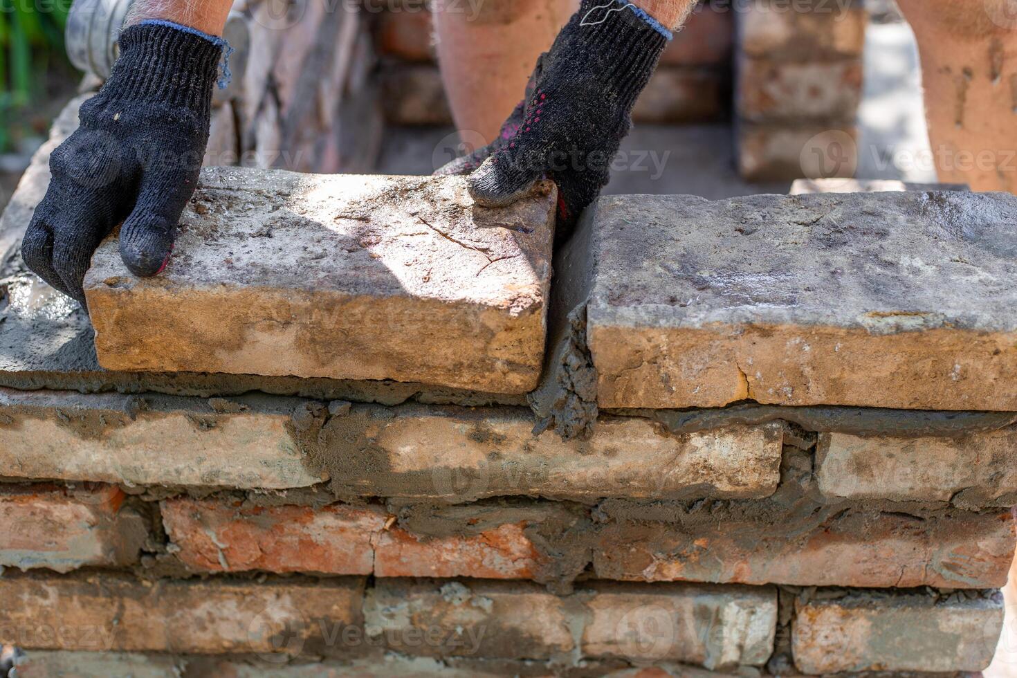 Two gloved hands laying bricks and mortar on a partially erected brick wall photo