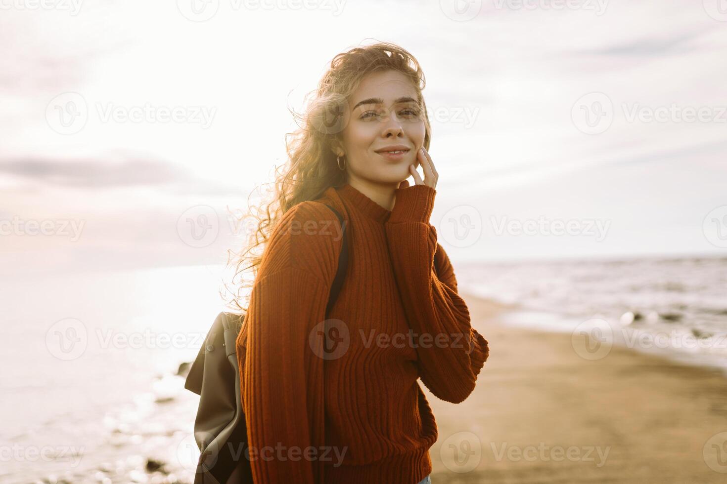 Woman enjoying breezy day near vibrant red lighthouse at sunset. Travel, lifestyle concept. photo