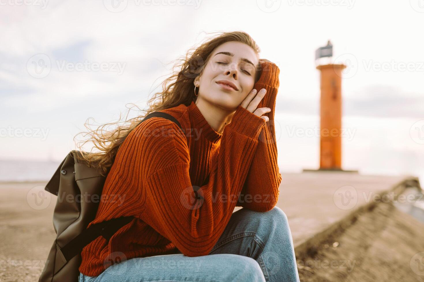Woman enjoying breezy day near red lighthouse at sunset. Travel, weekend, lifestyle concept. photo