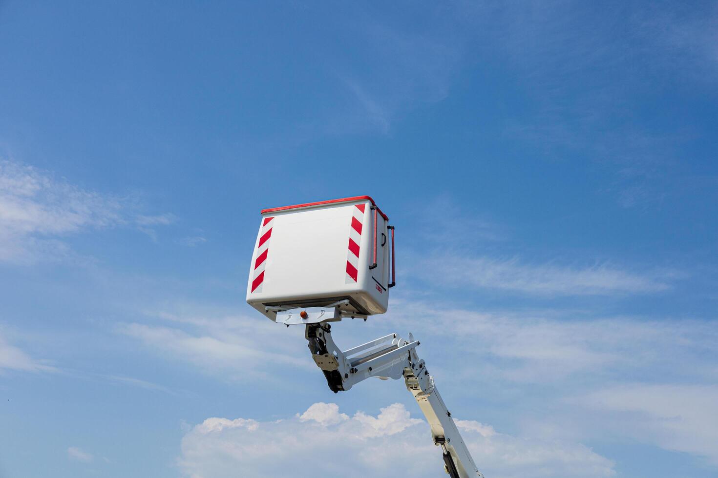 A tall work platform is lifted high, showcasing its reach against a bright, sunny sky with scattered clouds photo