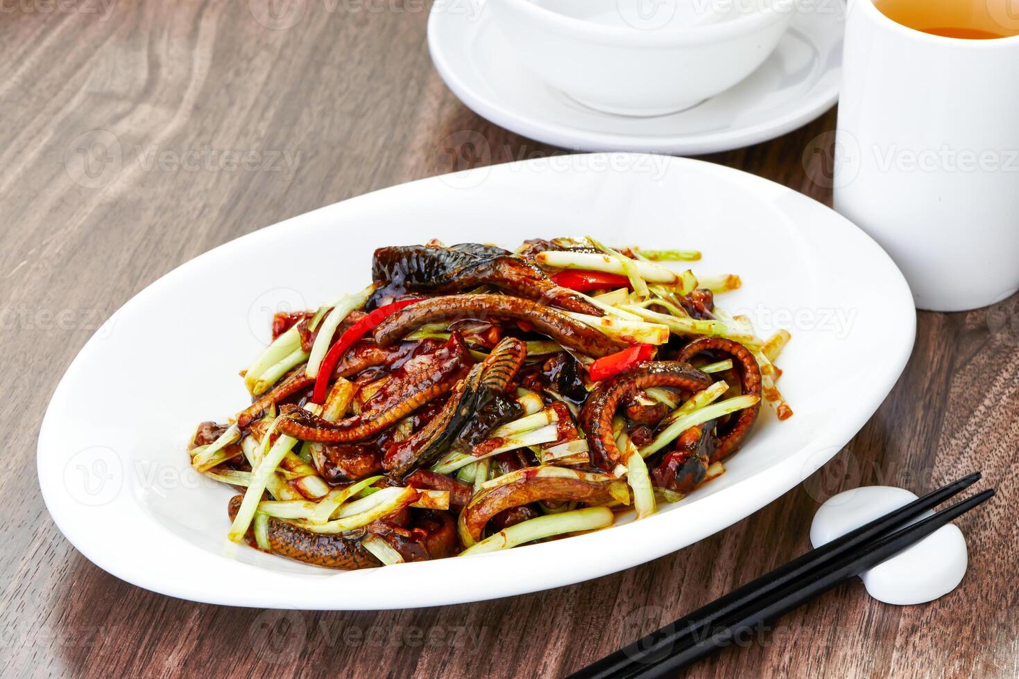 Delicious Fried Eel with Chives and Peppers with chopsticks served in plate side view of Authentic Asian Dish photo