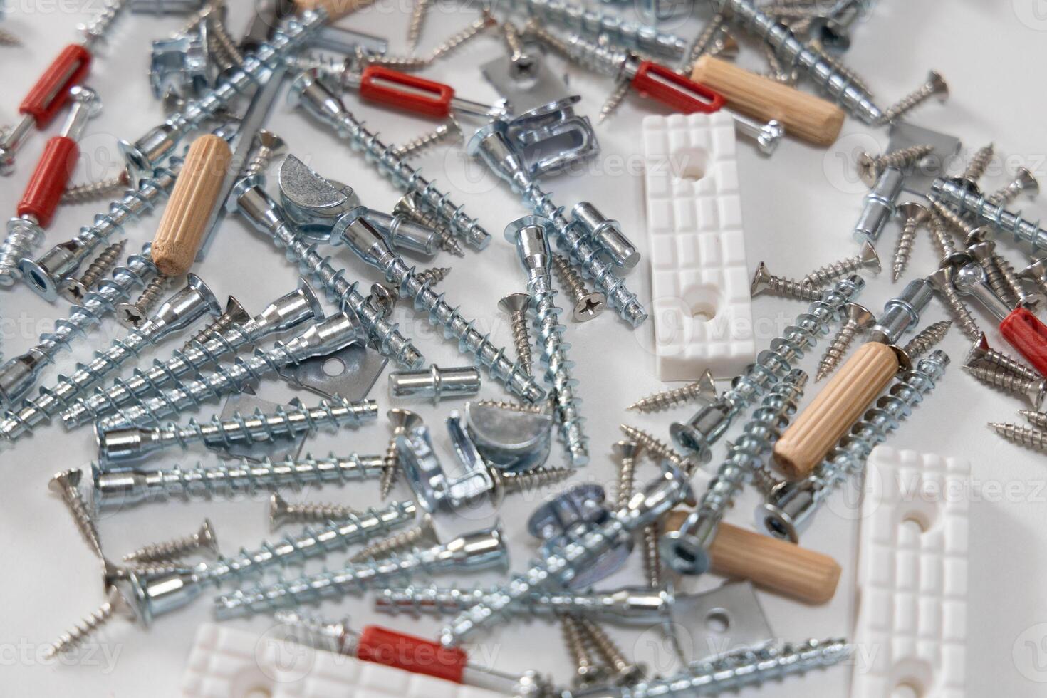 A variety of screws, bolts, and furniture hardware scattered on a white background. Ideal for concepts of assembly, repair, and home improvement. photo