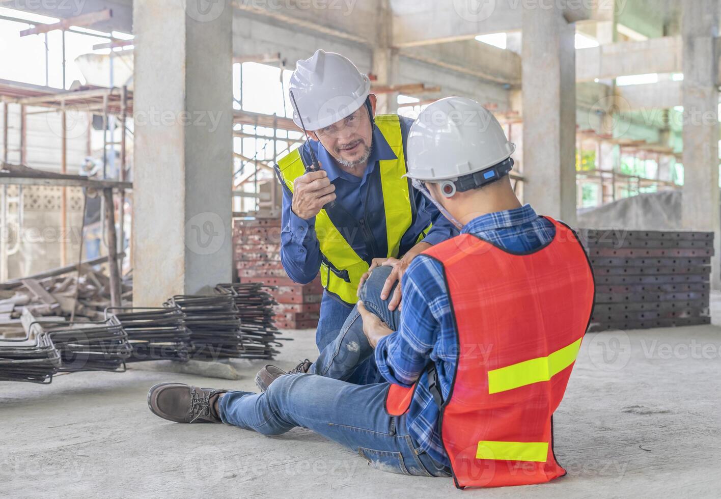 construction worker wears safety gear sitting on floor using walkie talkie call first aid team to help an accident worker at site,concept of risk management,accident in site work photo