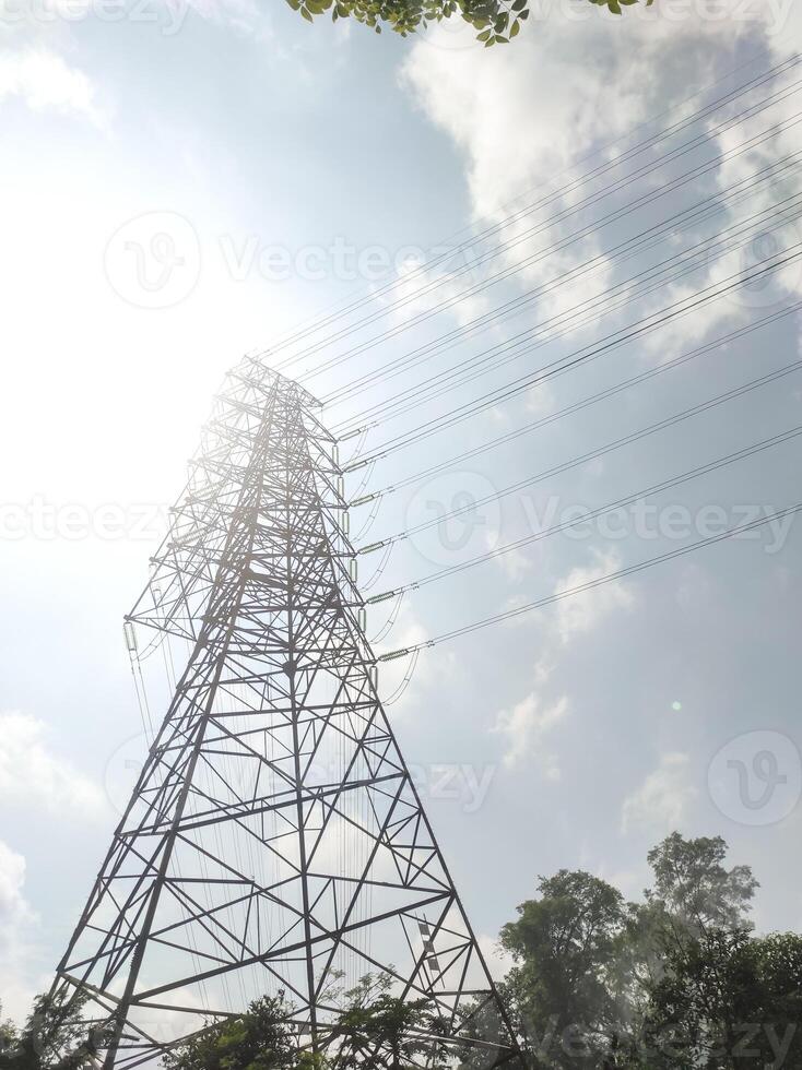 Low-angle shot of an Ultra High Voltage Power Line tower. An electrical distribution tower with bright sunlight, few clouds, and a clear sky in the background. Electrical technology industry. photo
