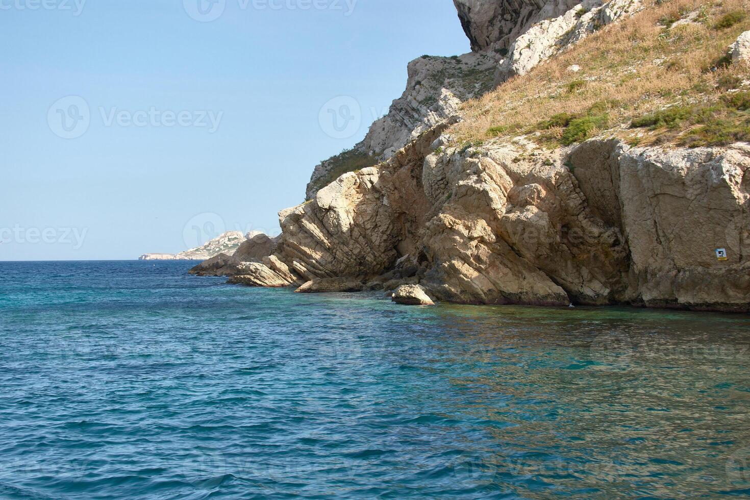 Boat cruising the Mediterranean next to the Calanques of Marseille, with a clear sky and rock formations in the background photo