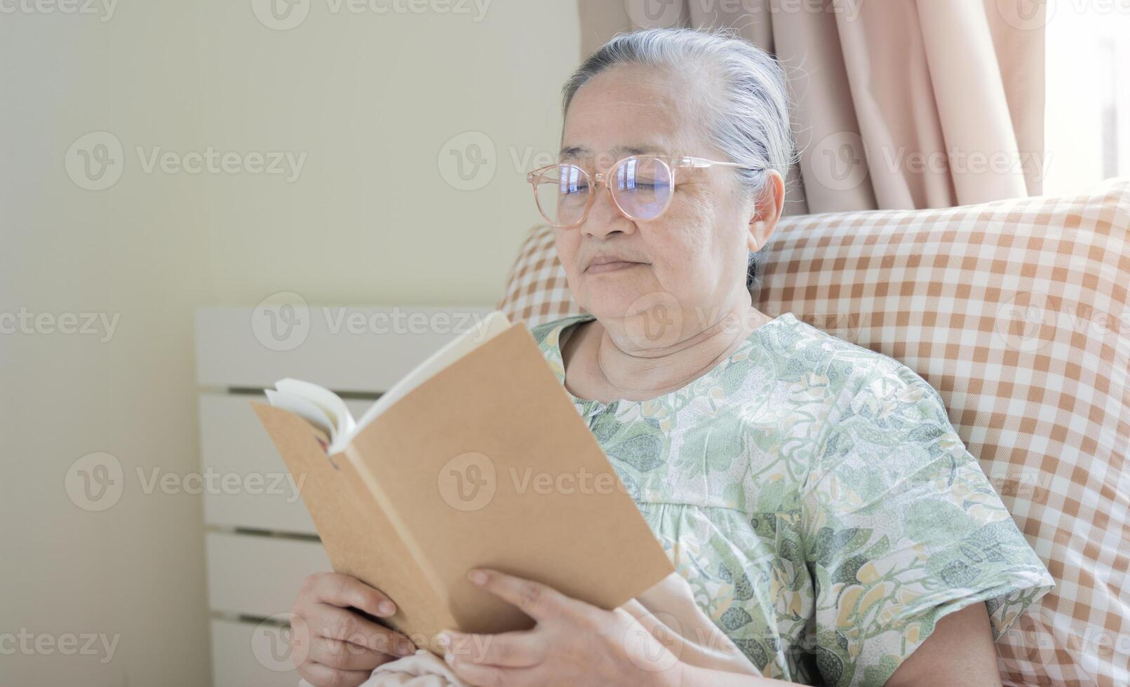 Refreshed elderly 60s female wakes up in morning, reading book, seated in bed in bedroom photo