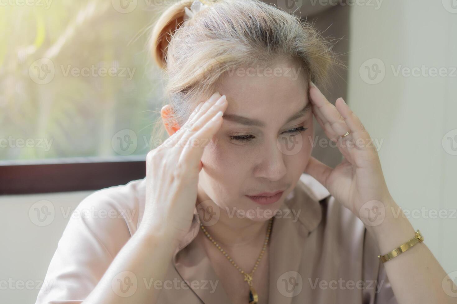 Adult beautiful Asian woman sitting nearby the window and suffering from headache desperate, stressed photo