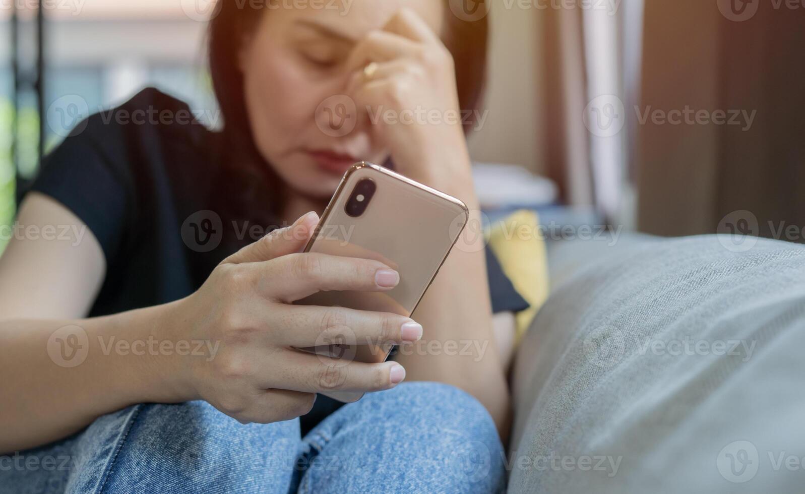 A beautiful adult Asian woman sitting one sofa with smart phone and feeling sad. photo