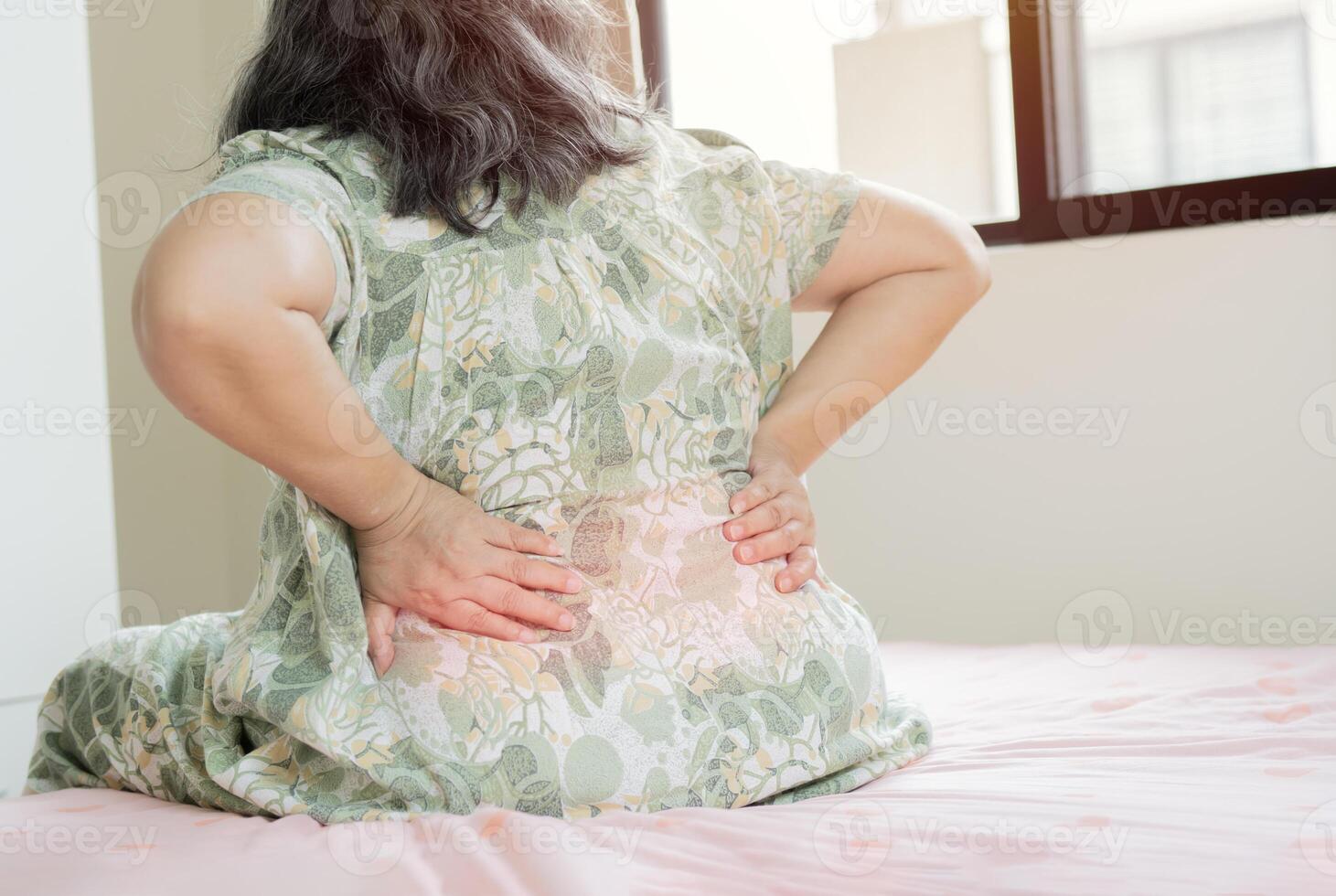 Old female sitting on bed touching lower back feeling discomfort photo