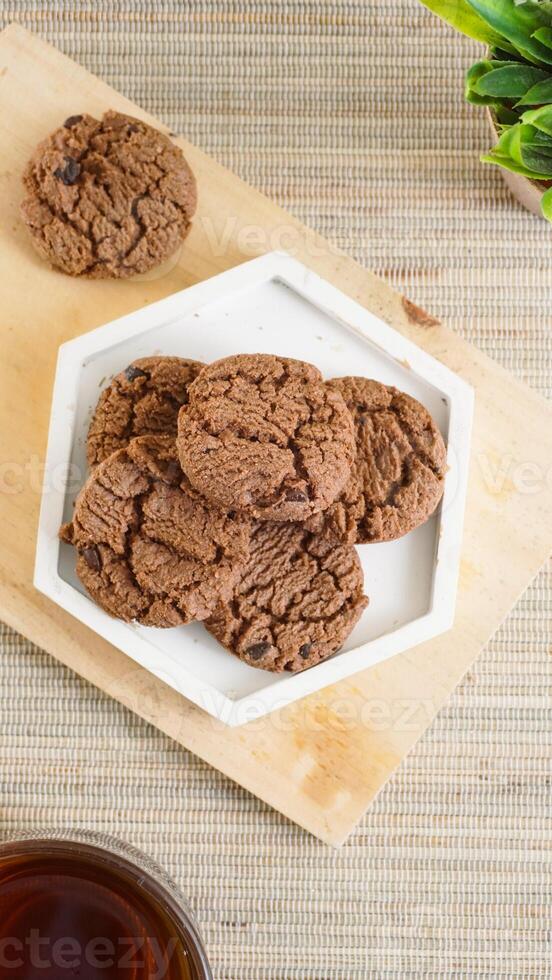 Top view of chocolate cookies treats on a white plate with a cup tea isolated on wooden textured background photo