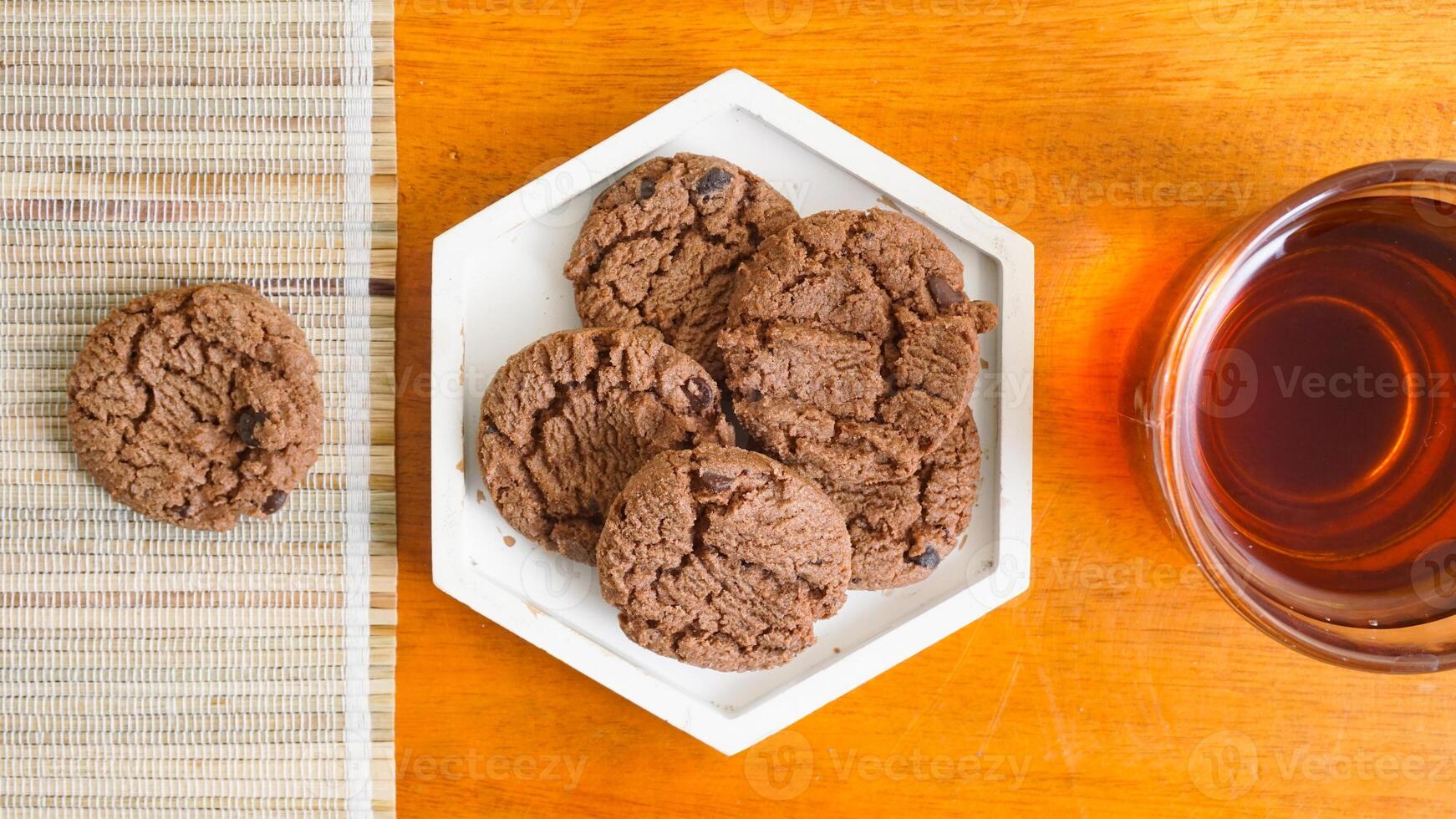 Top view of chocolate delicious chips cookies on a white plate with a cup of tea isolated on wooden textured background photo