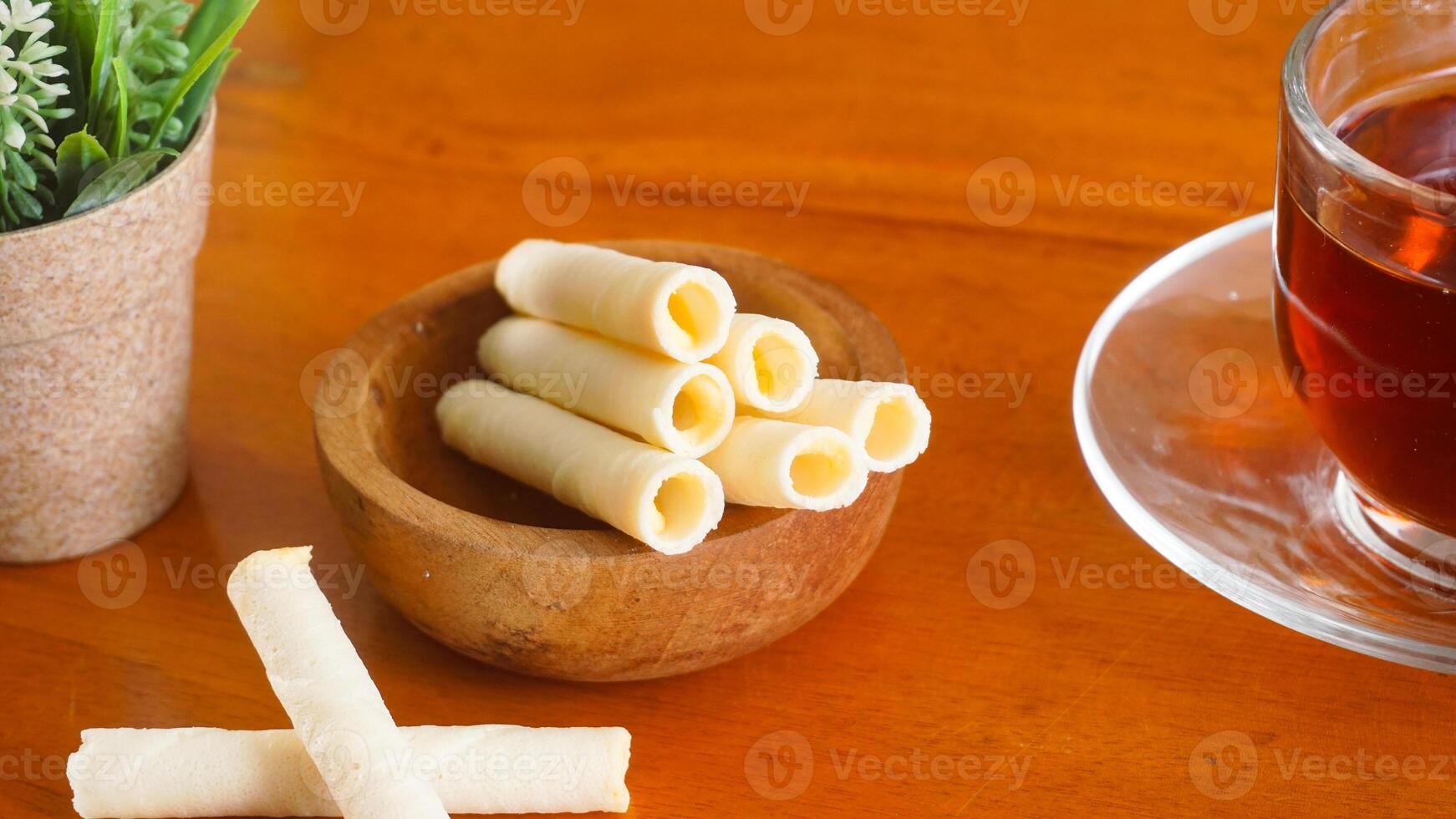Delicious wafer snack rolls with sweet cheese cream filling serving on plate with a cup of tea isolated on wooden background photo