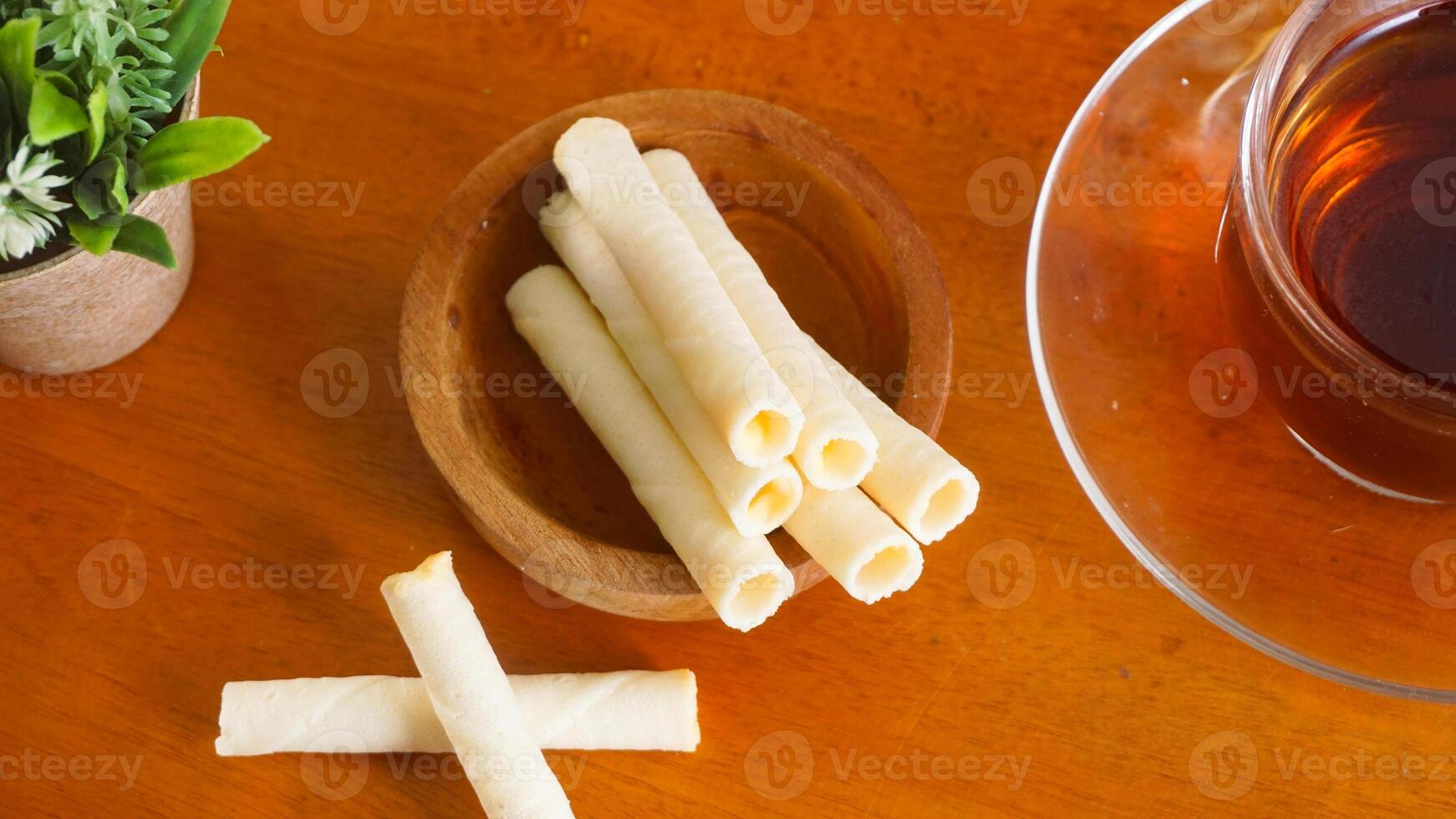 Wafer snack rolls with sweet cheese cream filling serving on plate with a cup of tea for enjoyment isolated on wooden background photo