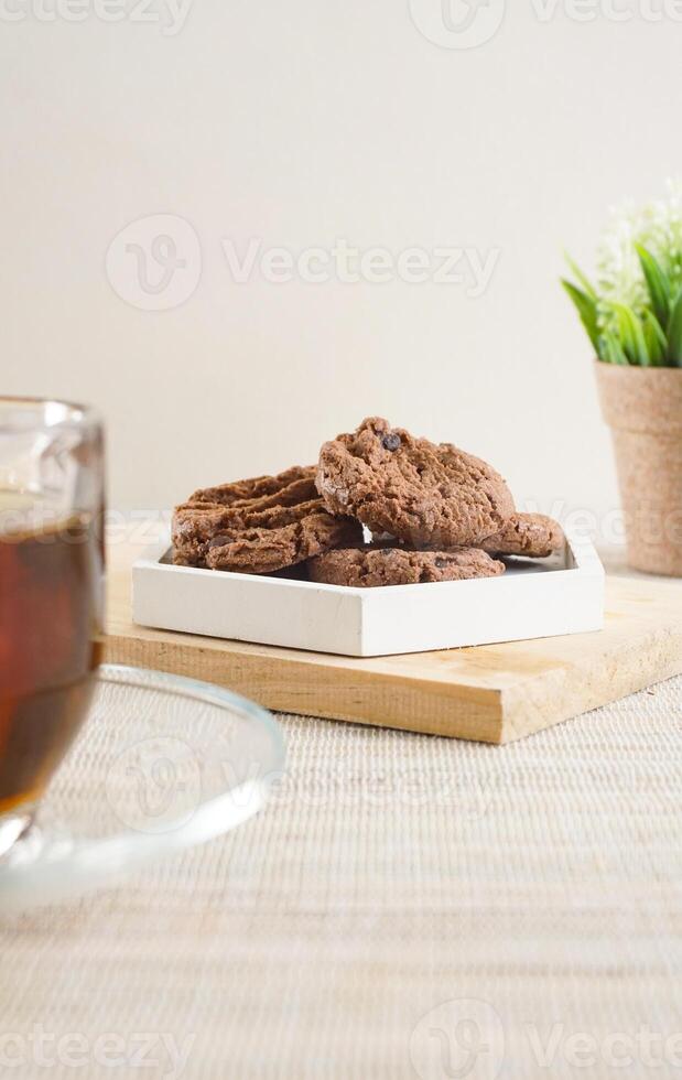 Chocolate cookies treats on a white plate with a cup tea isolated on wooden textured background photo