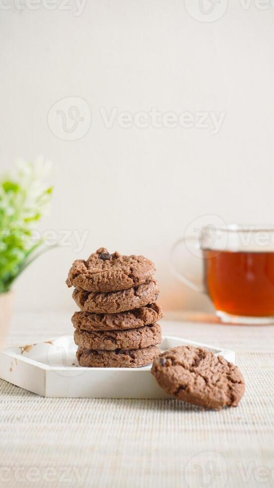 Stack of chocolate cookies on a white plate with a cup of tea isolated on light background photo