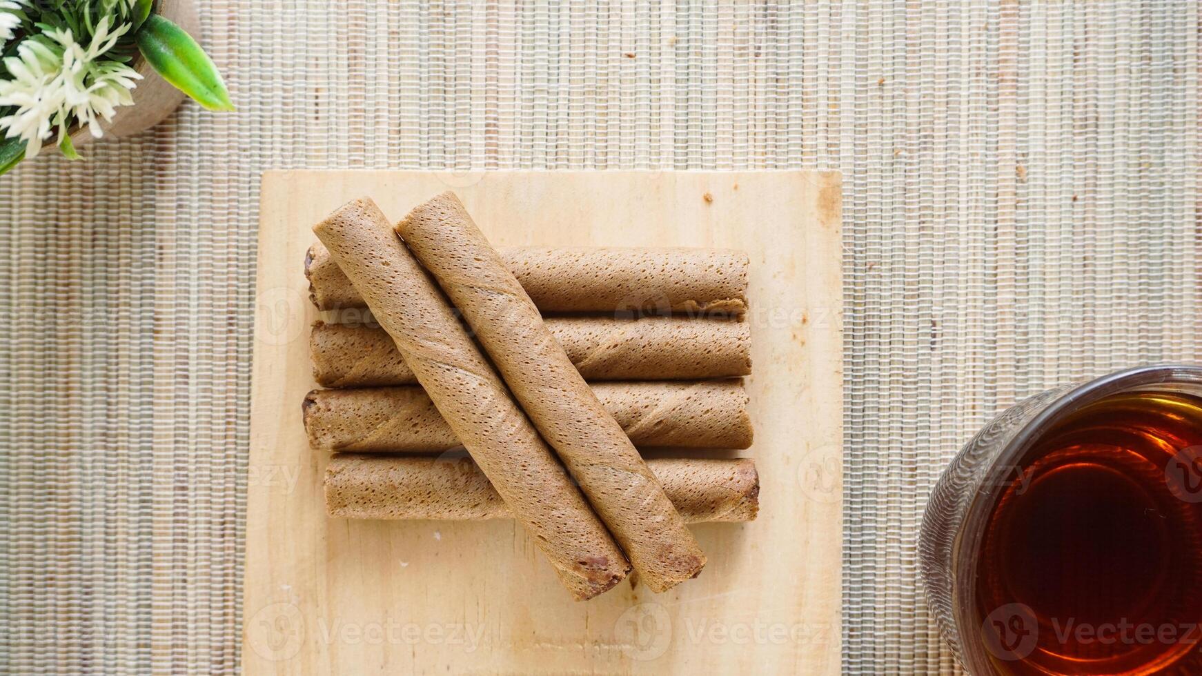 Top view of crispy chocolate wafer roll on a wooden board with a cup of tea isolated on wooden textured background photo