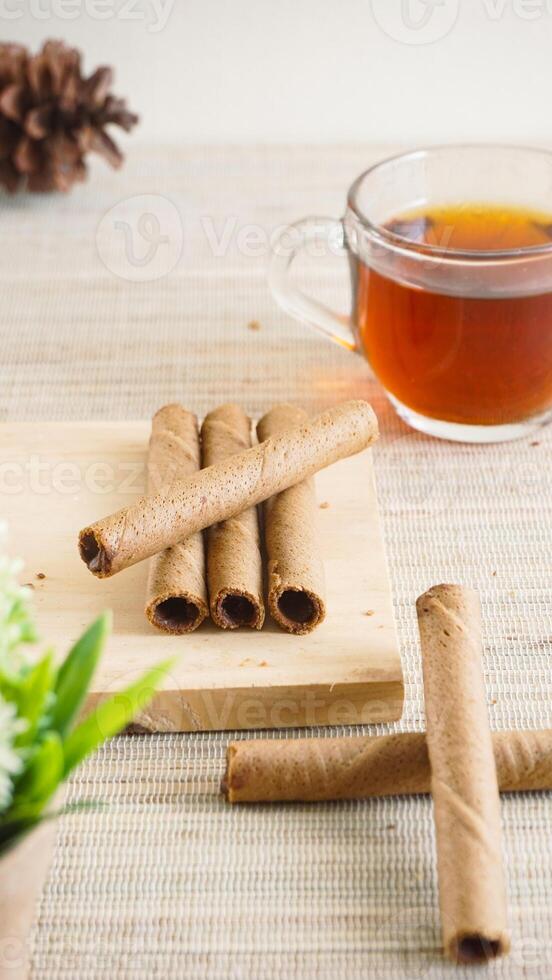 Delicious chocolate wafer roll on a wooden board with a cup of tea for enjoyment isolated on wooden textured background photo