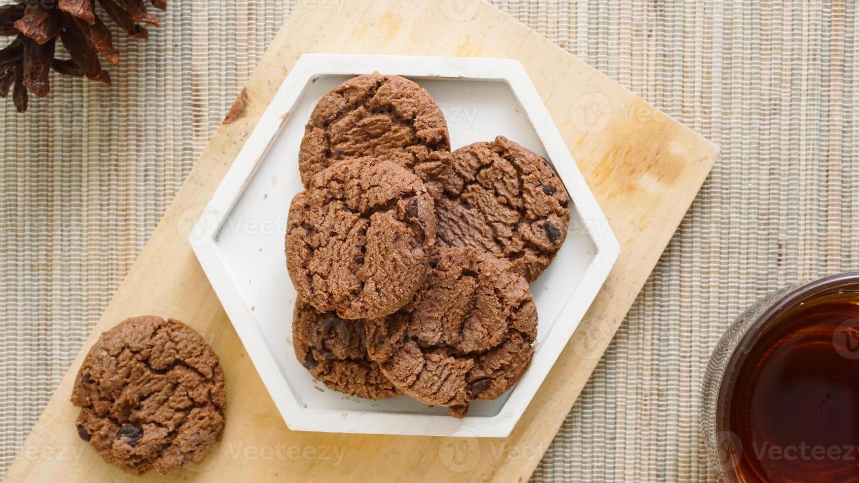 Top view of sweet chocolate cookies on a white plate with a cup tea isolated on wooden textured background photo