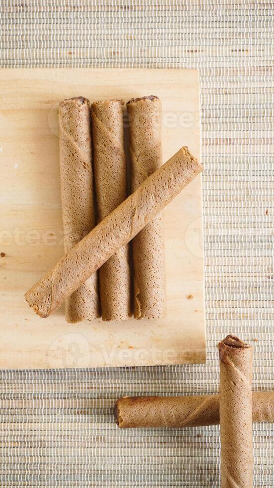 Top view of delicious chocolate wafer roll on a wooden board isolated on wooden textured background photo