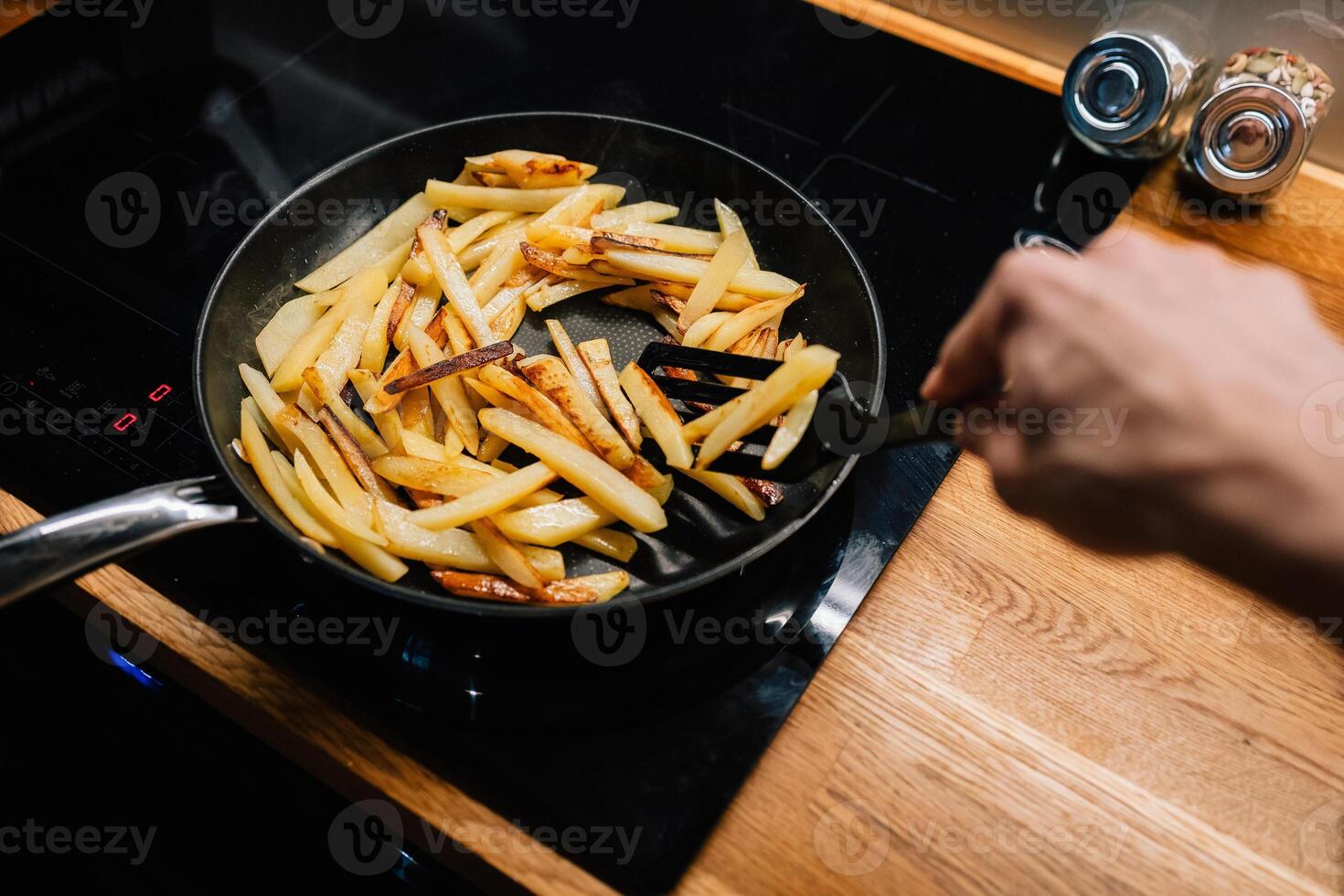 Chef is using spatula to turn batch of golden french fries cooking in non stick pan on modern cooktop, ensuring even browning and crispy texture. Chef turning golden french fries in non stick pan. POV photo