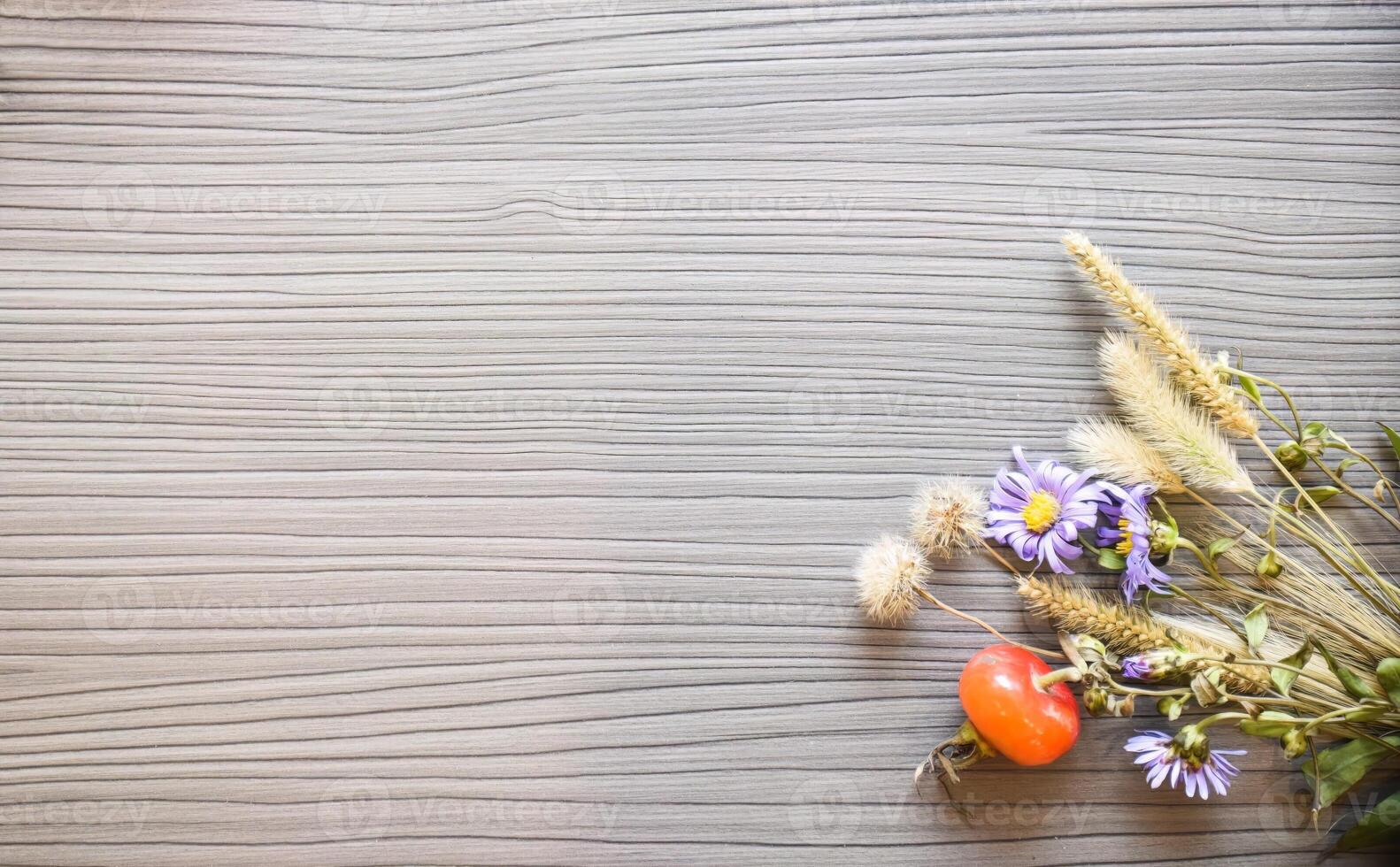 Autumn wooden background with wild flowers, grass and berries of hawthorn, rose hips in the lower right corner. Copy space photo