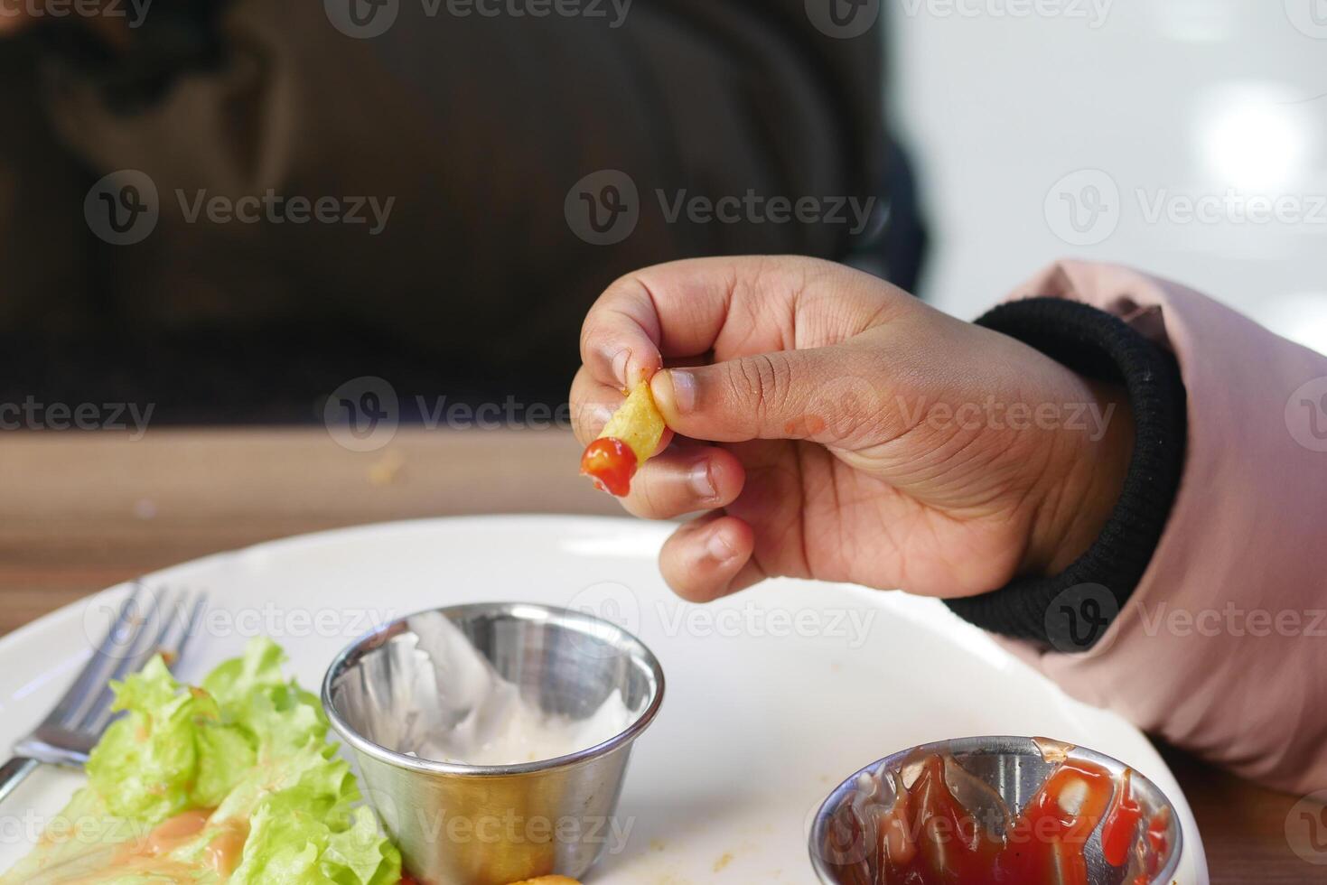 A young hand holds a french fry topped with ketchup while sitting photo