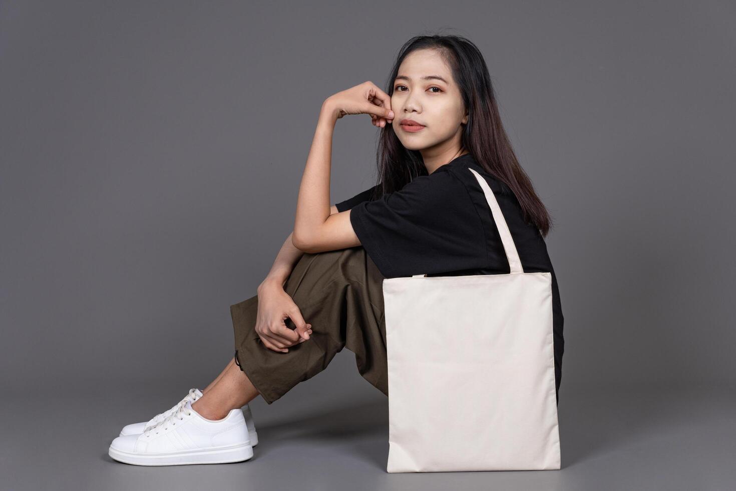 Female Sitting on Floor Holding Blank Canvas Tote Bag, Eco-Friendly Reusable Fabric with Handle, Close-Up Mockup, No Plastic and Environmental Concept Background photo
