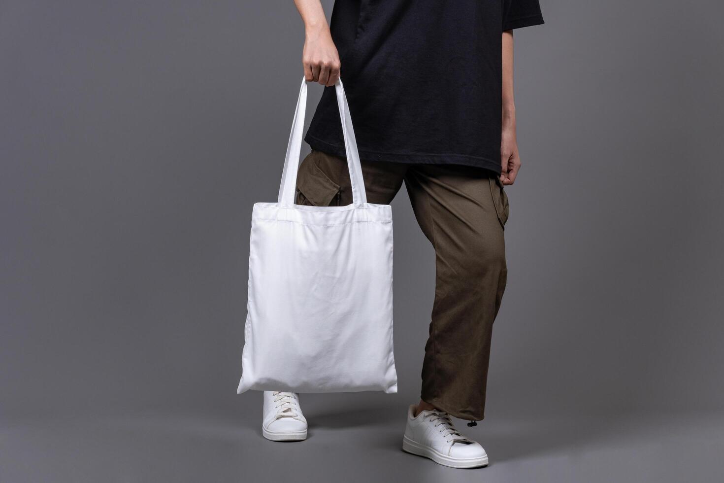 Female Walking While Holding Blank Canvas Tote Bag, Eco-Friendly Reusable Fabric with Handle, Close-Up Mockup, No Plastic and Environmental Concept photo