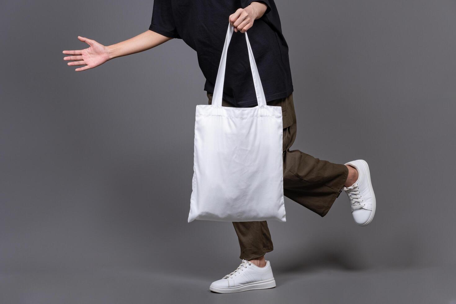 Woman Walking While Holding Blank Canvas Tote Bag, Eco-Friendly Reusable Fabric with Handle, Close-Up Mockup, No Plastic and Environmental Concept photo