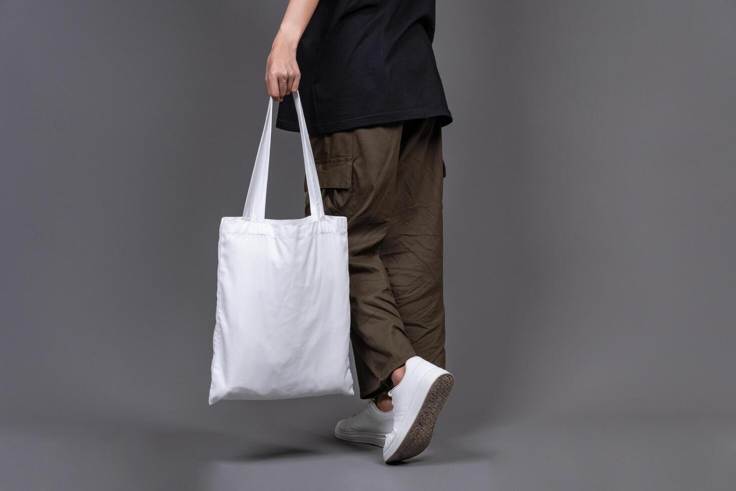 Female Walking While Holding White Canvas Tote Bag, Eco-Friendly Reusable Fabric with Handle, Close-Up Mockup, No Plastic and Environmental Concept photo