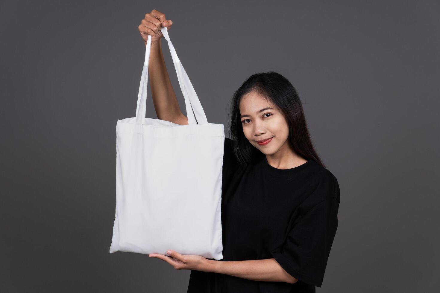 Front View of Woman Holding Blank Canvas Tote Bag, Eco-Friendly Reusable Fabric with Handle, Close-Up Mockup, No Plastic and Environmental Smiling photo